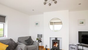 A modern living room with a grey sofa, a fireplace, a round mirror, and a TV. - Mynydd Mwyn (Llanfairpwllgwyngyll)