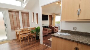 A modern kitchen with wooden cabinets, a dining area with a table and chairs, and a living area with a sofa and a TV.