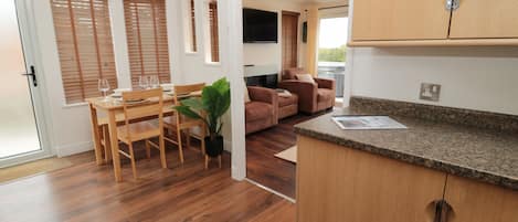 A modern kitchen with wooden cabinets, a dining area with a table and chairs, and a living area with a sofa and a TV.