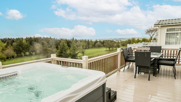 A hot tub on a wooden deck with a view of a grassy field and trees.