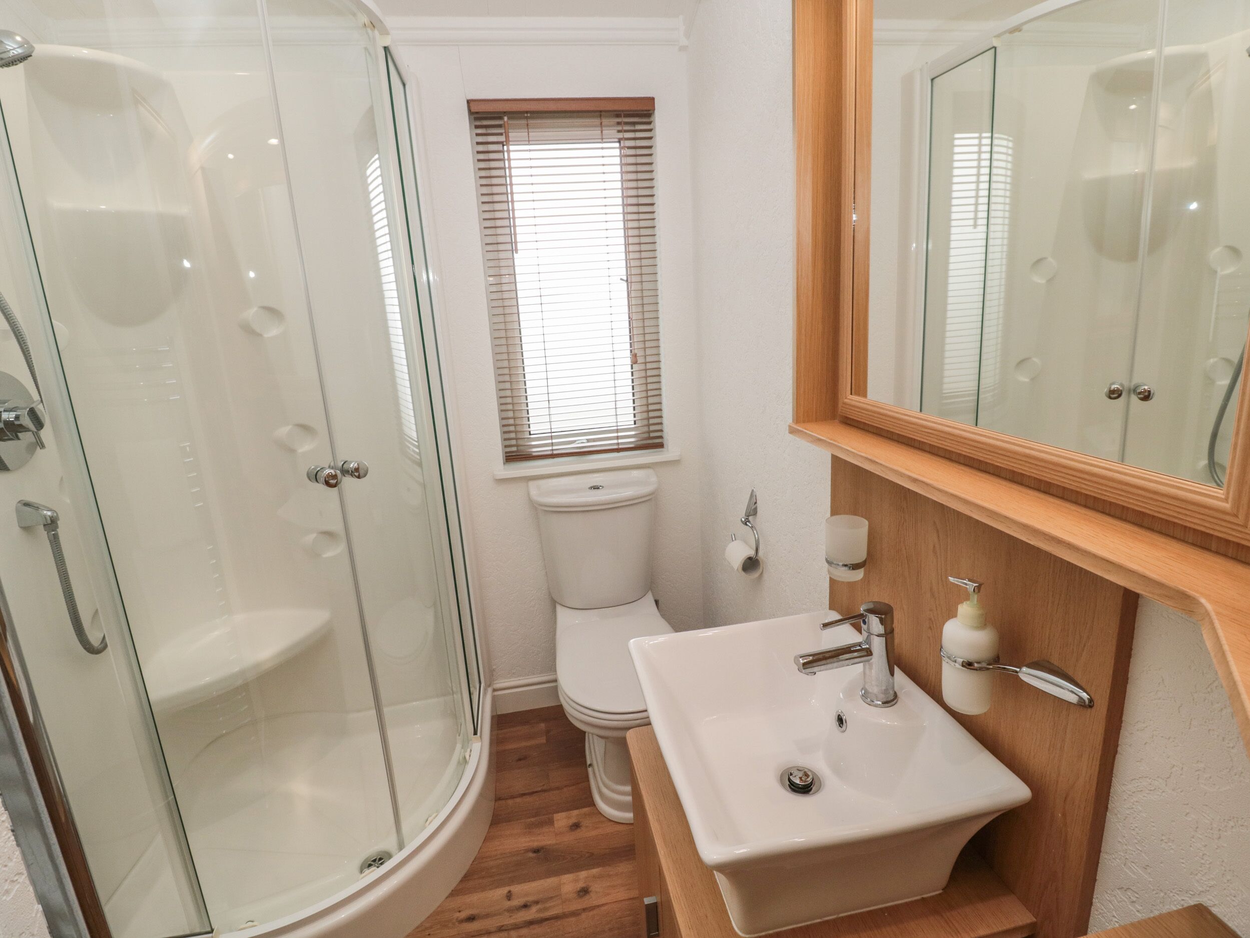 A bathroom with a glass-enclosed shower, a toilet, and a sink with a wooden vanity.