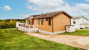 A single-story wooden mobile home with a porch and a small attached shed.