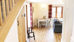 A wooden staircase leading to a dining area with a white table and chairs, a grey sofa, and plaid curtains. - The Cider House (Leominster)