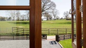 A view through a wooden-framed window of a grassy field with a gravel path leading to a wooden gate. - The Cider House (Leominster)