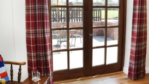 A wooden door with a glass panel, flanked by red plaid curtains, leading to an outdoor patio with metal chairs and a brick wall. - The Cider House (Leominster)