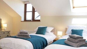 A hotel room with two beds, each with a blue blanket and a folded towel. There is a window with a view of the outside, and a nightstand with a lamp on each bed. - The Cider House (Leominster)