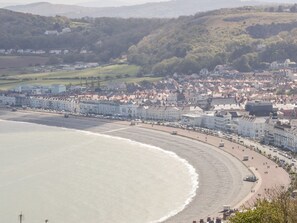 A coastal town with a beach, buildings, and hills in the background. - 4 Anglesey Road (Llandudno)