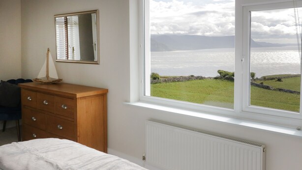 A bedroom with a bed, a dresser, a mirror, and a window with a view of the sea.