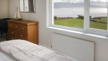 Quarto com cama, cômoda, espelho e janela com vista para o mar.