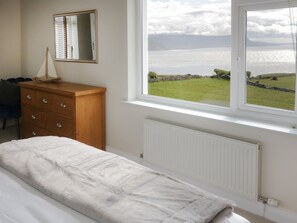 A bedroom with a bed, a dresser, a mirror, and a window with a view of the sea. - 4 Anglesey Road (Llandudno)