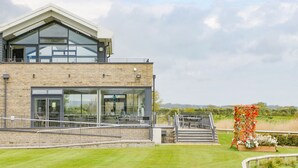 A modern building with a glass facade, a brick lower section, and a metal staircase leading to a covered outdoor area.