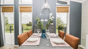 A dining area with a table set for four, two chairs on each side, a vase with flowers, and a hanging light fixture.