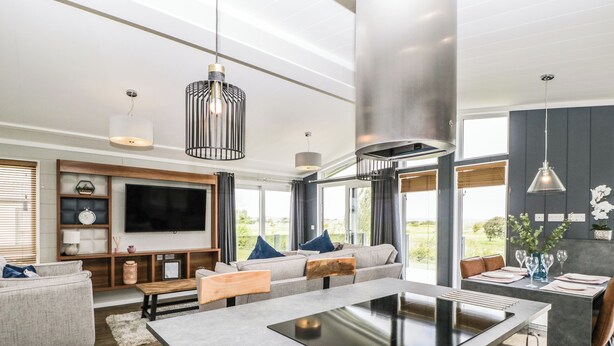A modern living room with a large TV, comfortable seating, a central island with a sink, and large windows offering a view.