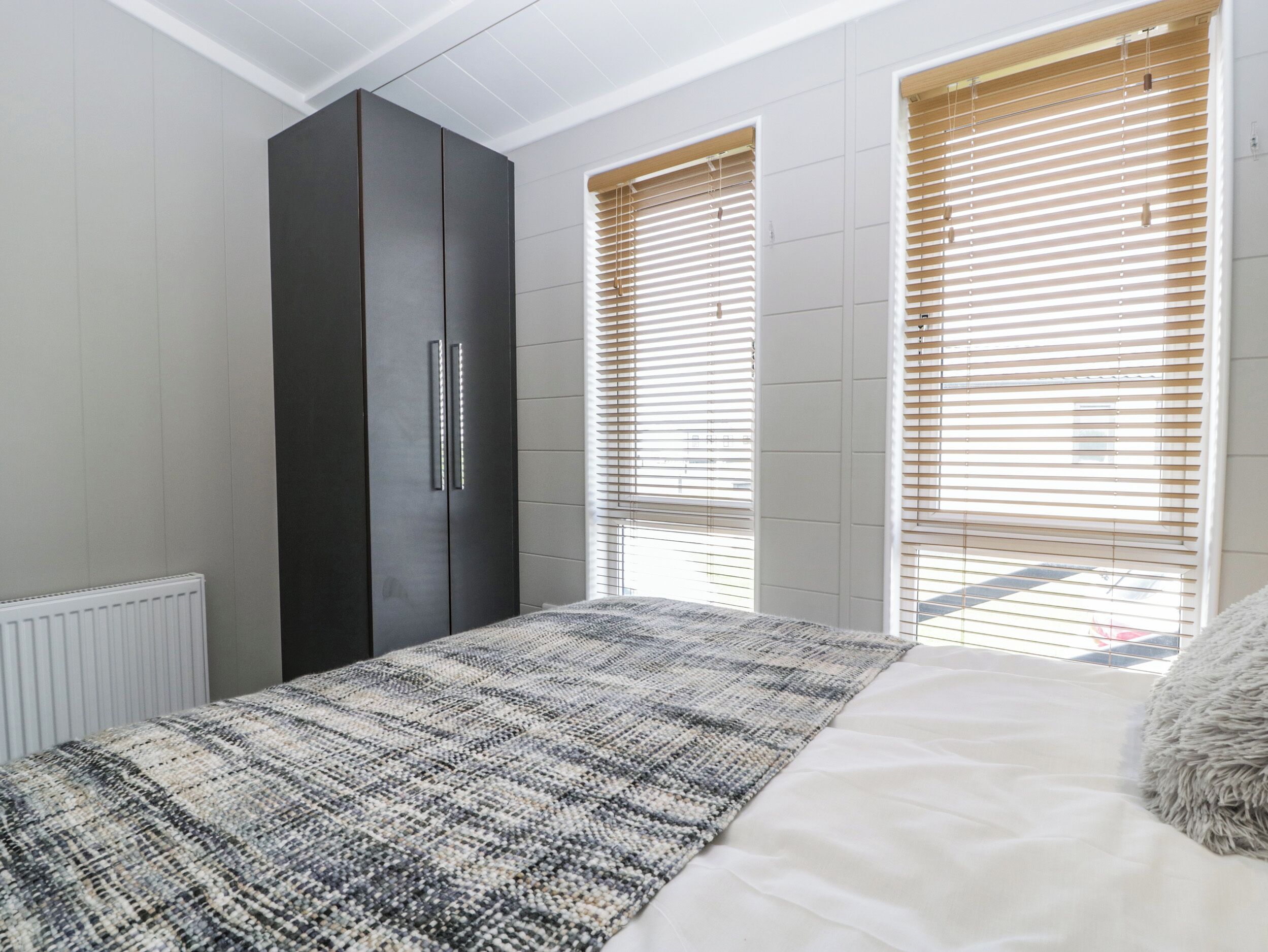Un dormitorio con cama, armario y dos ventanas con persianas.