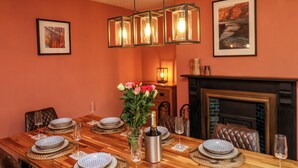 A dining area with a long wooden table set for six, featuring woven placemats, patterned plates, and a vase with flowers.