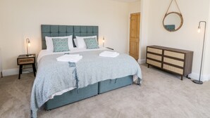 A bedroom with a bed, bedside tables, a dresser, a mirror, and a door.