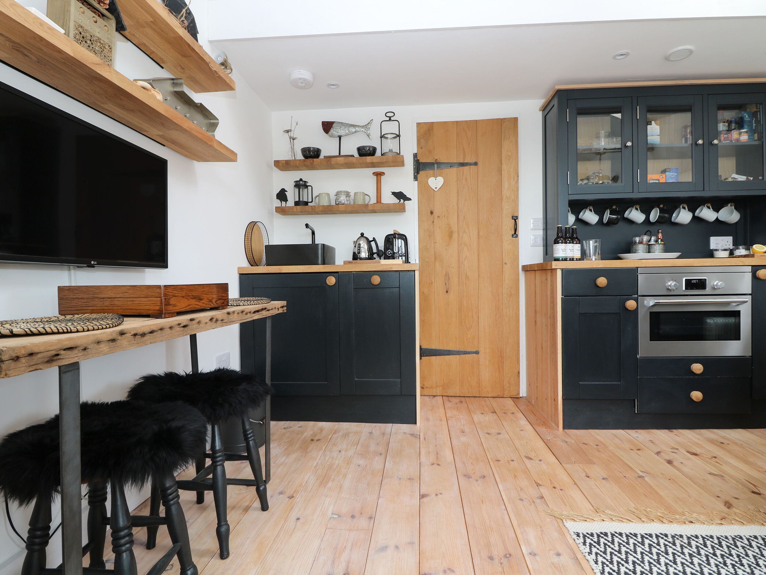 A modern kitchen with black cabinets, wooden countertops, and a built-in oven. There is a dining area with a round table and black chairs.