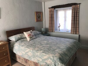 Une chambre à coucher comprenant un lit, une table de chevet, une commode, une fenêtre avec des rideaux et un tableau accroché au mur.