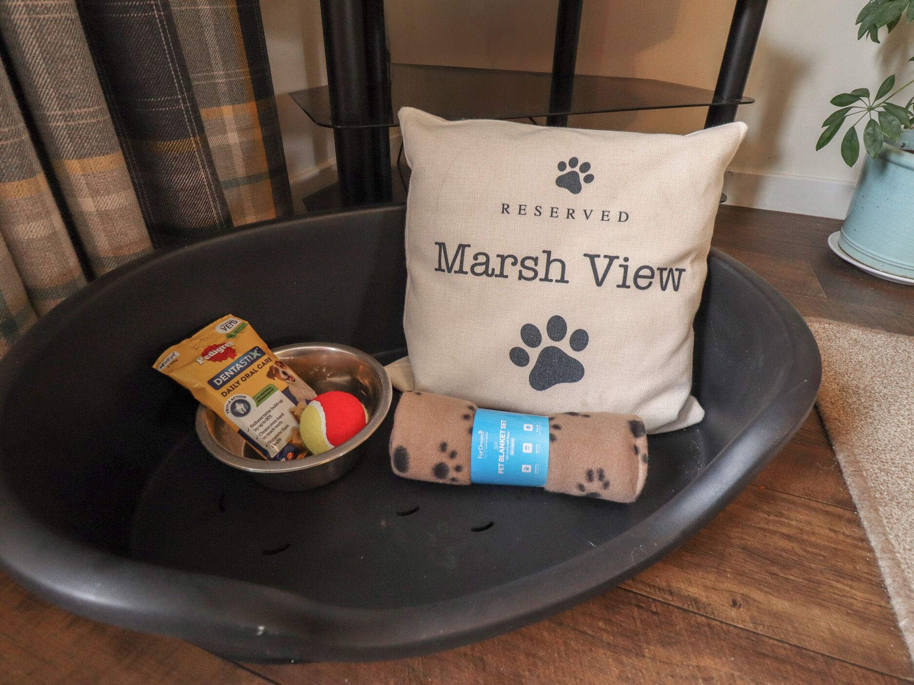 A pet bed with a pillow labeled "RESERVED Marsh View" and a bowl with pet food and a ball.
