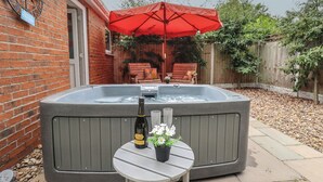 A hot tub with a red umbrella, a bottle of rose wine, and a small table with flowers.