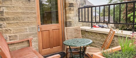 A wooden door, a small round table with chairs, and a potted plant on a balcony.