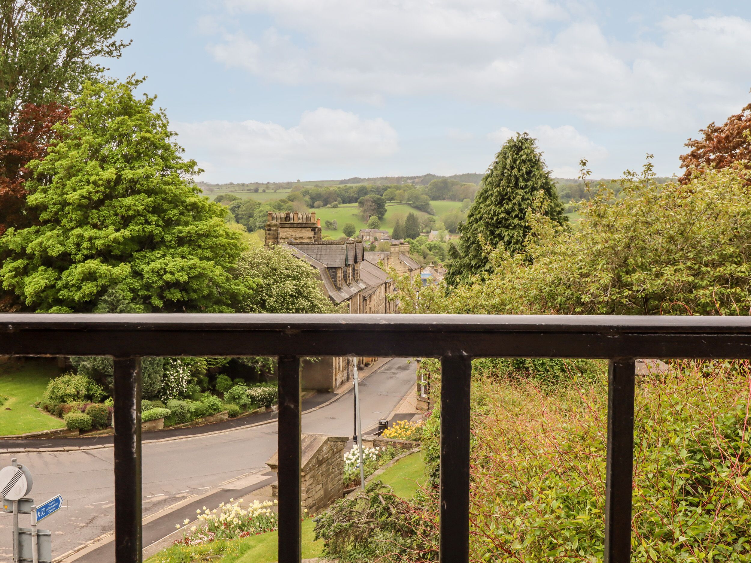 A view from a balcony overlooking a rural street with houses, greenery, and a clear sky.