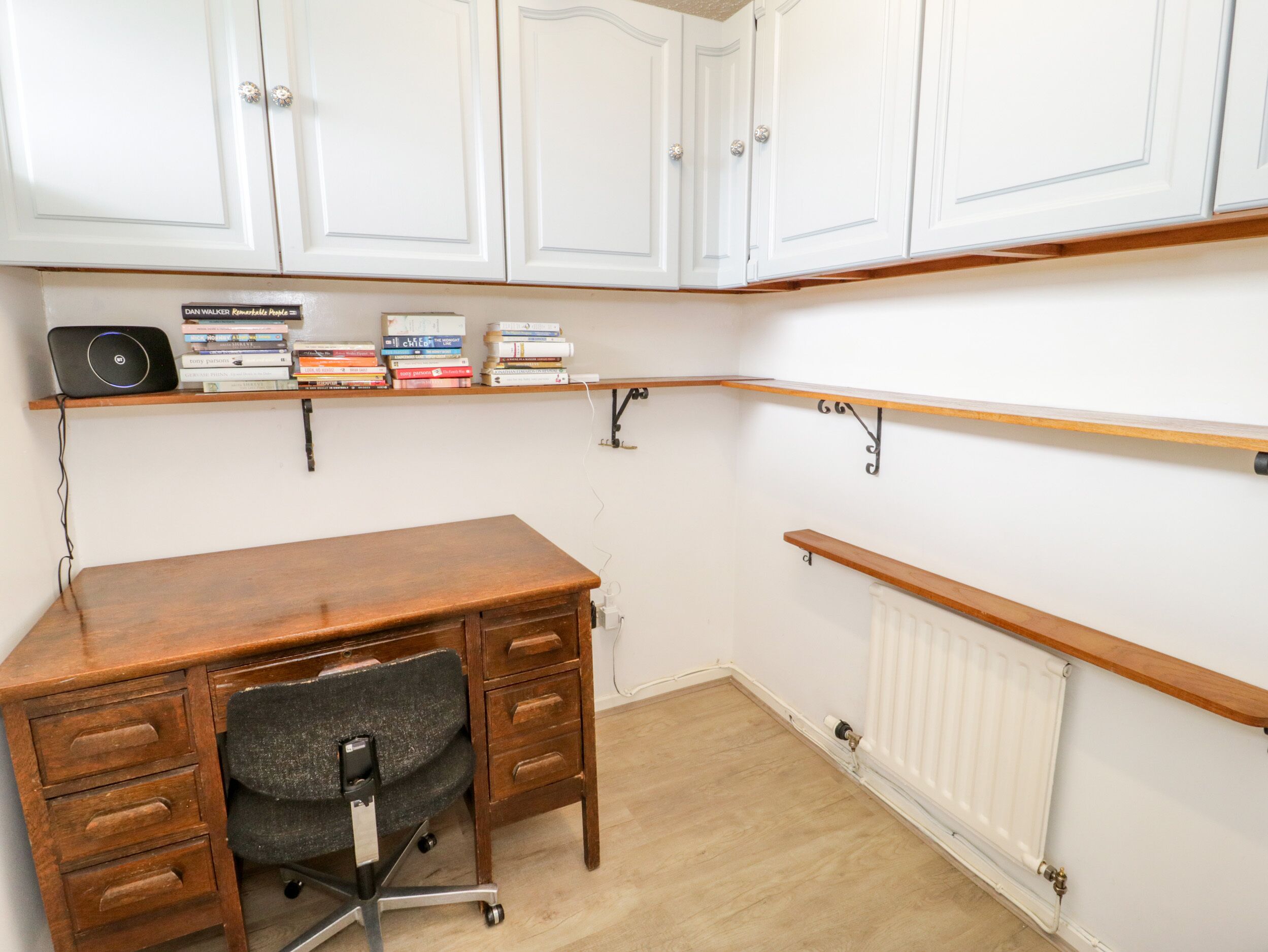 Ein Zimmer mit Schreibtisch, Stuhl, Heizkörper und weißen Schränken.