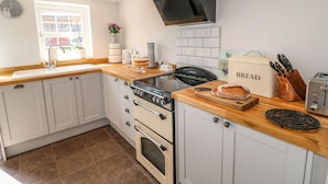 A modern kitchen with white cabinets, a wooden countertop, a stove, a toaster, and a bread box. - Hillcrest (Retford)