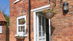 A brick house with a white door, a welcome mat, and a potted plant. - Hillcrest (Retford)
