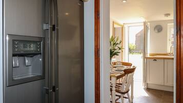 A modern kitchen with a stainless steel refrigerator, a dining table with chairs, and a view of the outside through a window.