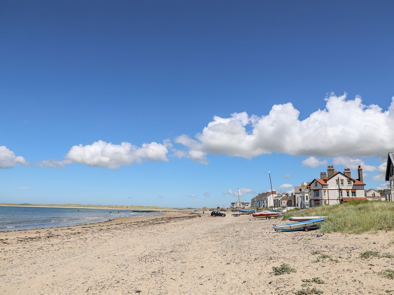 A beach with boats, a lighthouse, and a row of houses.