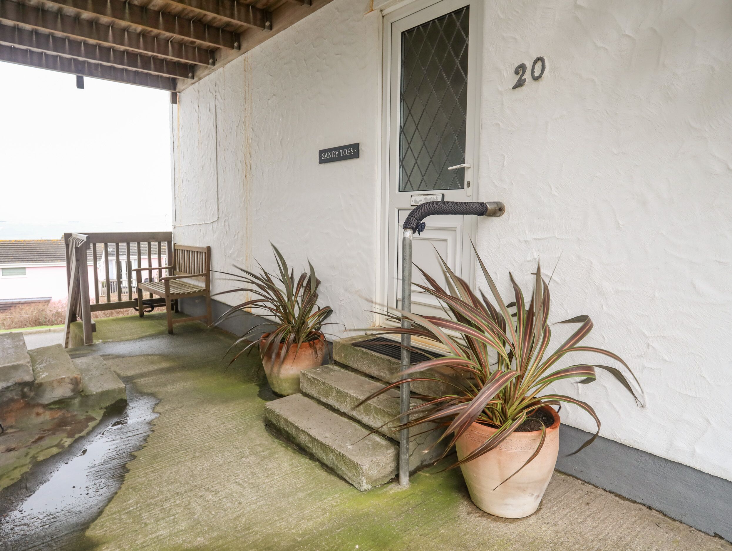 A building entrance with a white door, a sign reading "SANDY TOES", and two potted plants.