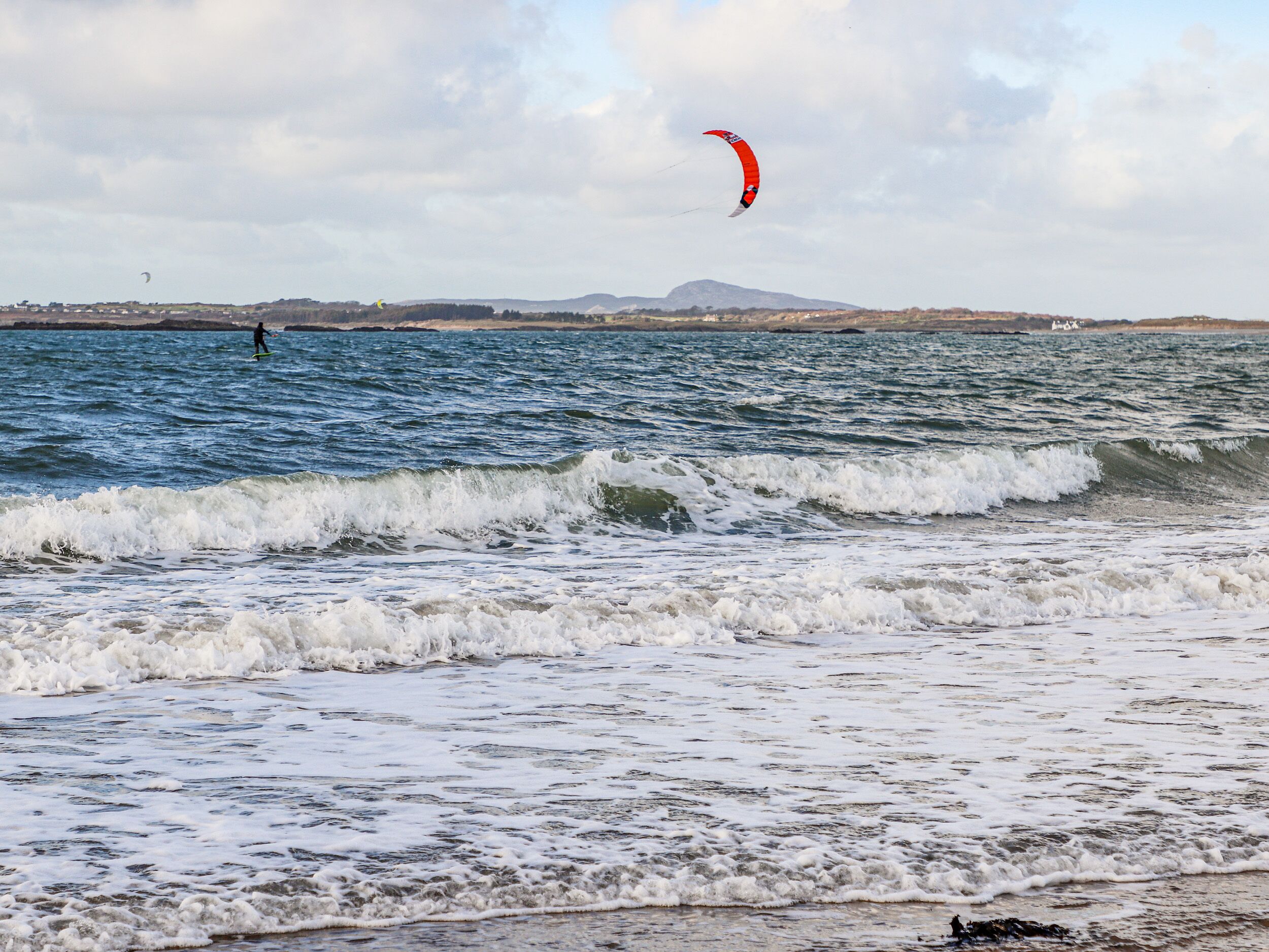 Escena costanera amb onades i una persona fent kitesurf.