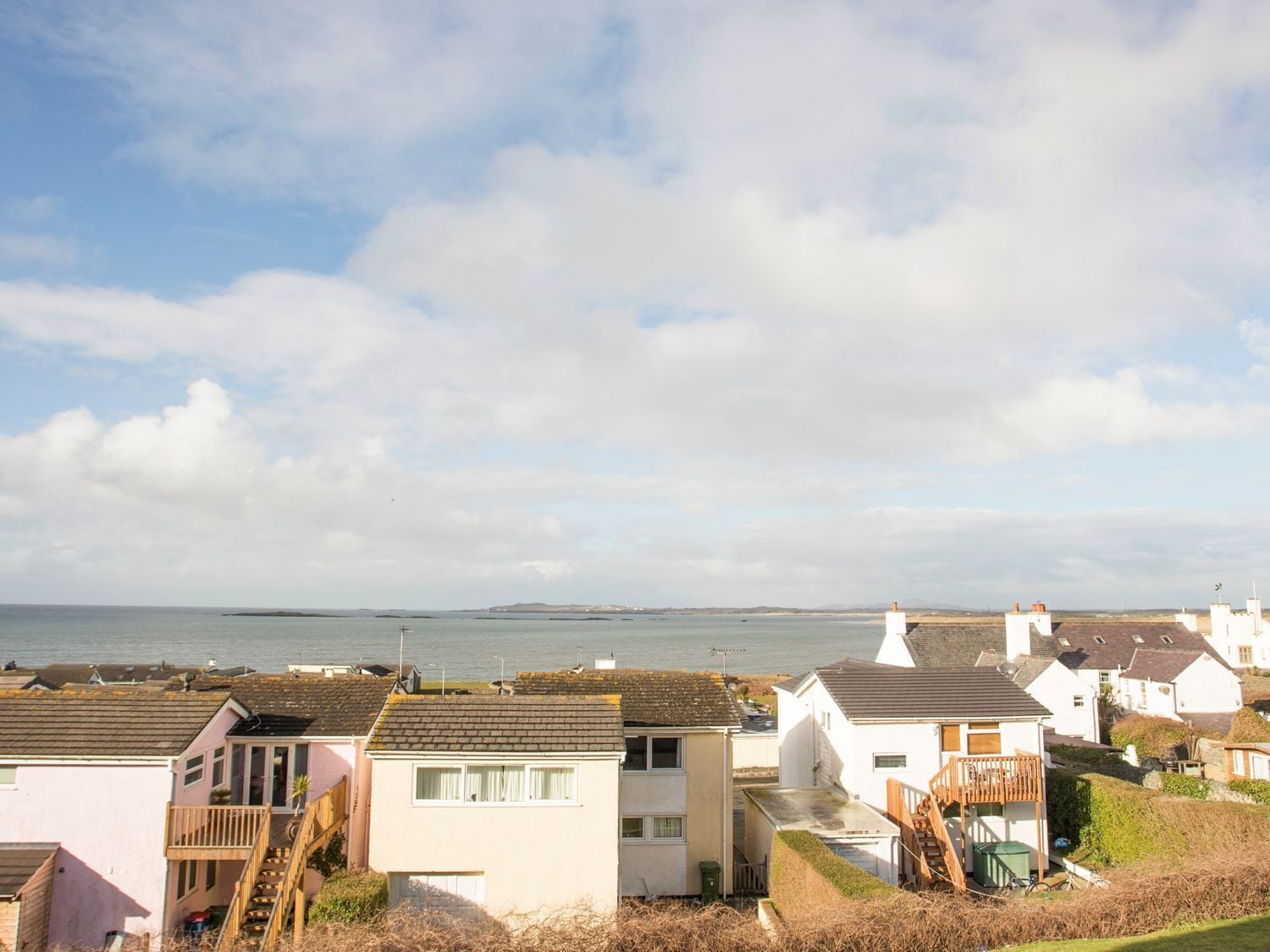 A coastal residential area with houses, a view of the sea, and a clear sky.