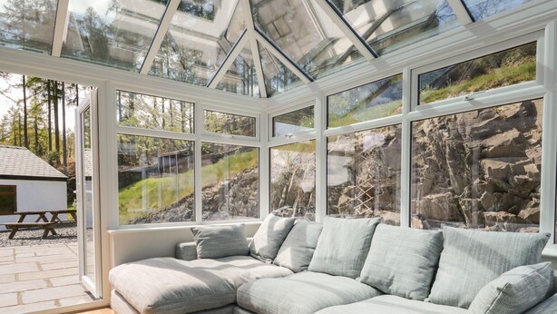 Ein modernes Wohnzimmer mit einer großen Eckcouch, einer Glasdecke und Blick auf eine felsige Landschaft.