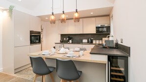 A modern kitchen with a central island, two black chairs, and pendant lighting. - Vale Lodge (Pewsey)