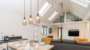 A modern kitchen with a dining area, a gray sofa, and a TV mounted on the wall. - Vale Lodge (Pewsey)