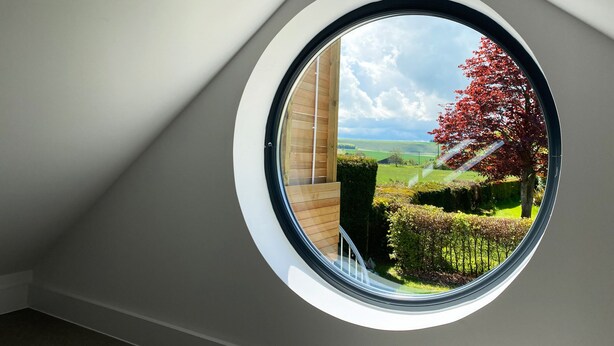 A skylight with a view of a red-leaved tree and a green field. - Vale Lodge (Pewsey)