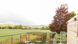 A balcony with two wooden chairs, a metal railing, and a view of a green field and trees. - Vale Lodge (Pewsey)