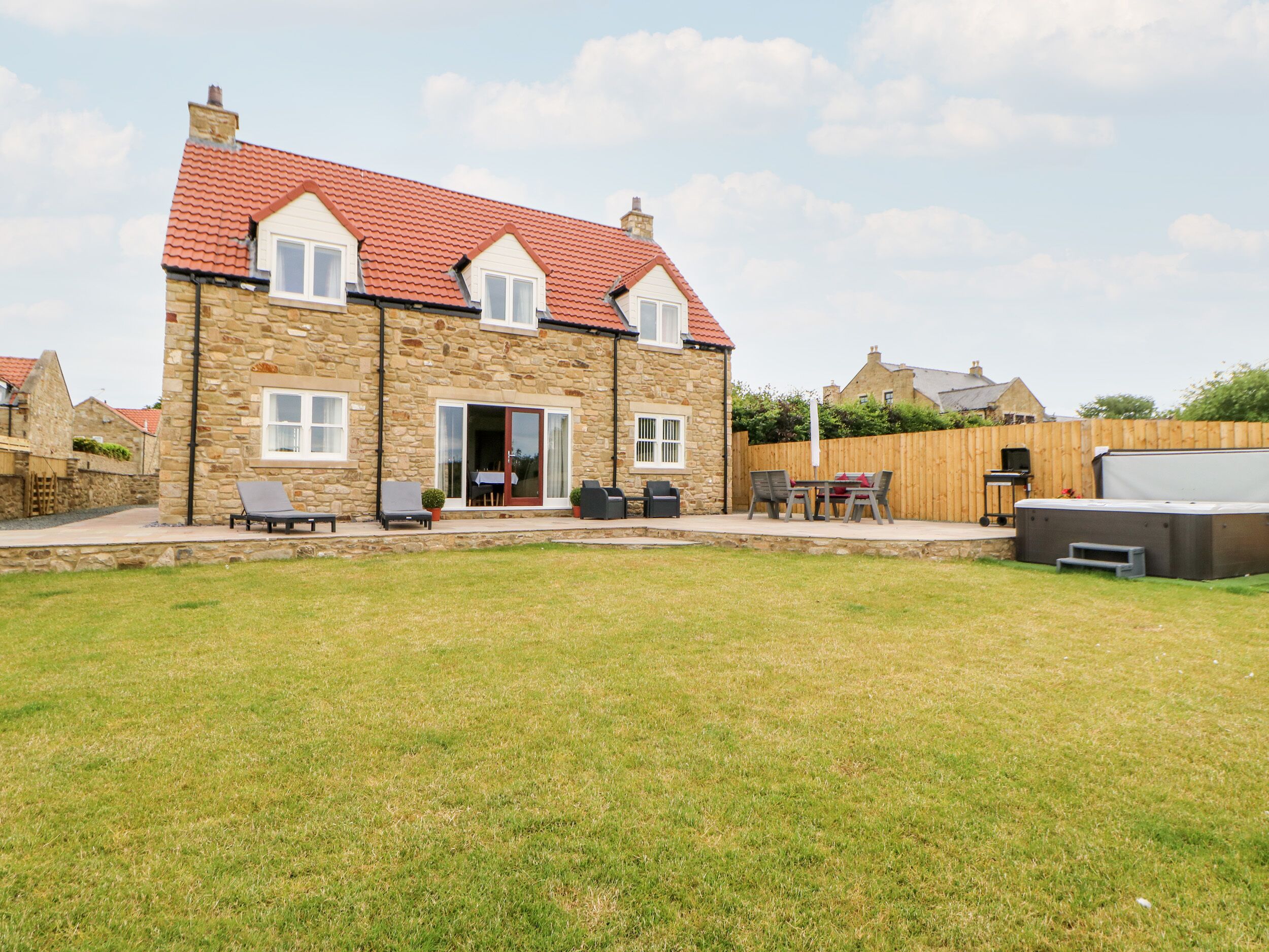 A stone house with a red-tiled roof, a patio with outdoor furniture, and a barbecue area.