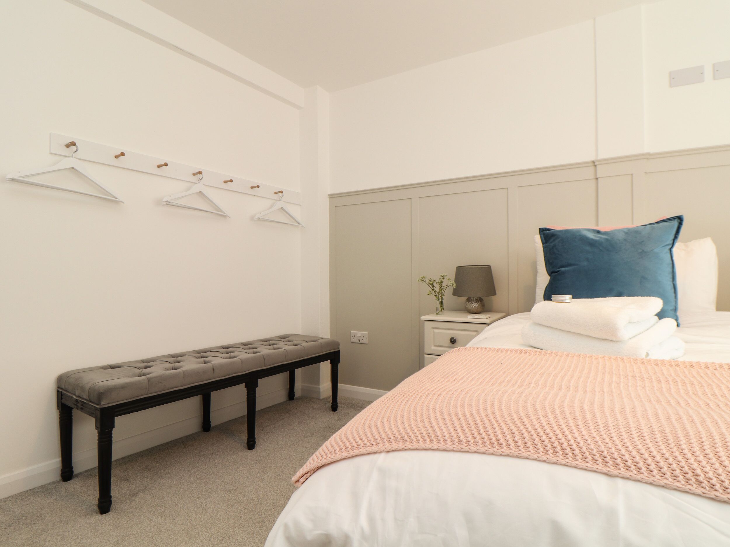 A bedroom with a bed, a bench, a nightstand, and a wall-mounted coat rack.