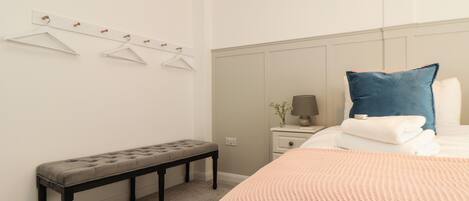 A bedroom with a bed, a bench, a nightstand, and a wall-mounted coat rack.