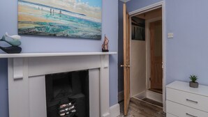 A hallway with a white fireplace, a painting of a beach scene, and a wooden door leading to another room. - Poppy Cottage (Deal)