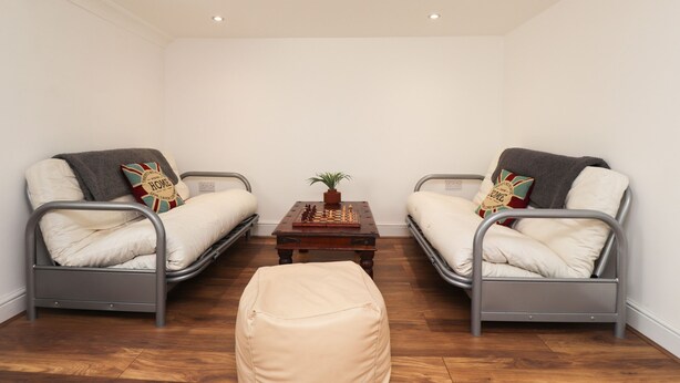 A room with two metal-framed beds, a small wooden table with a chessboard, and a single potted plant.