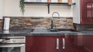 A kitchen with a stone backsplash, a stainless steel sink, and a red cabinet. - Poppy Cottage (Deal)