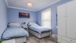 A bedroom with two beds, a nightstand, a lamp, a wardrobe, and a painting on the wall.