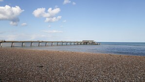 A pebbled beach with a pier extending into the water. - Poppy Cottage (Deal)