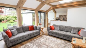 Un salon spacieux avec deux canapés gris, un plafond en bois et une vue sur un jardin et une cuisine.