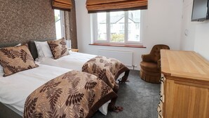 Une chambre avec deux lits, une commode en bois, une chaise et une fenêtre avec des rideaux.