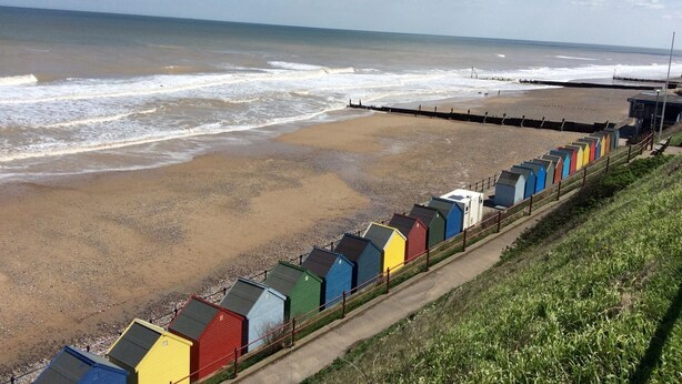 A beach with colorful beach huts along the shore and a pier extending into the water. - 20 Siesta Mar (Norwich)